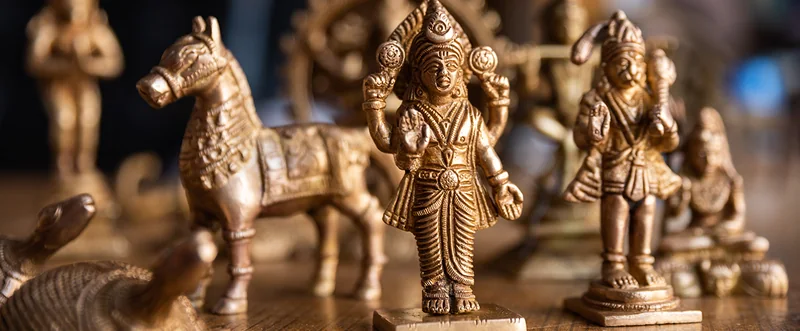 धातु की घोड़े और देव आकृतियां एक पंक्ति में रखी हैं; उनके आभूषणों और सतह पर बारीक नक्काशी दिखती है।